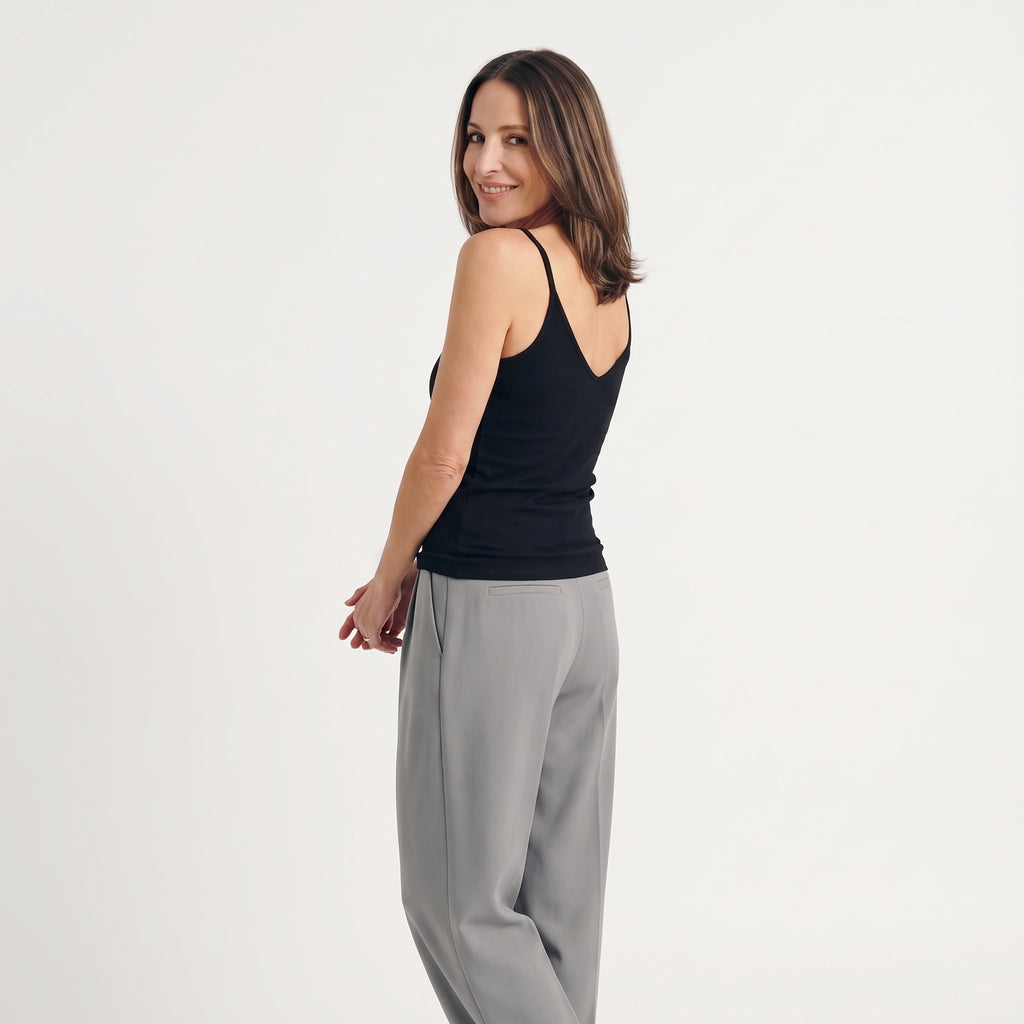 Black built-in bra camisole with a V-shaped back, worn with grey tailored pants, glancing back and smiling
