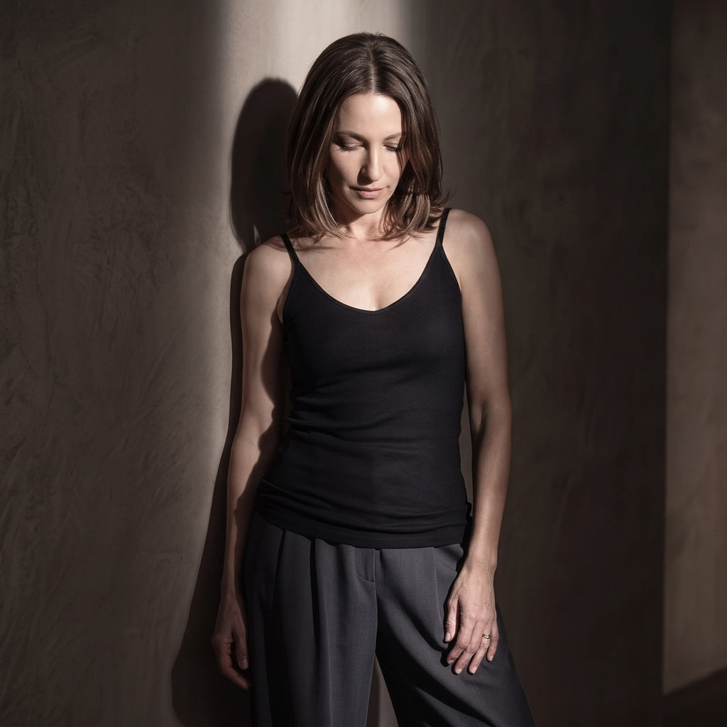 Black ribbed built-in bra camisole with dark grey pleated pants in low-key light, looking down