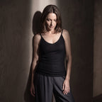 Black ribbed built-in bra camisole with dark grey pleated pants in low-key light, looking down