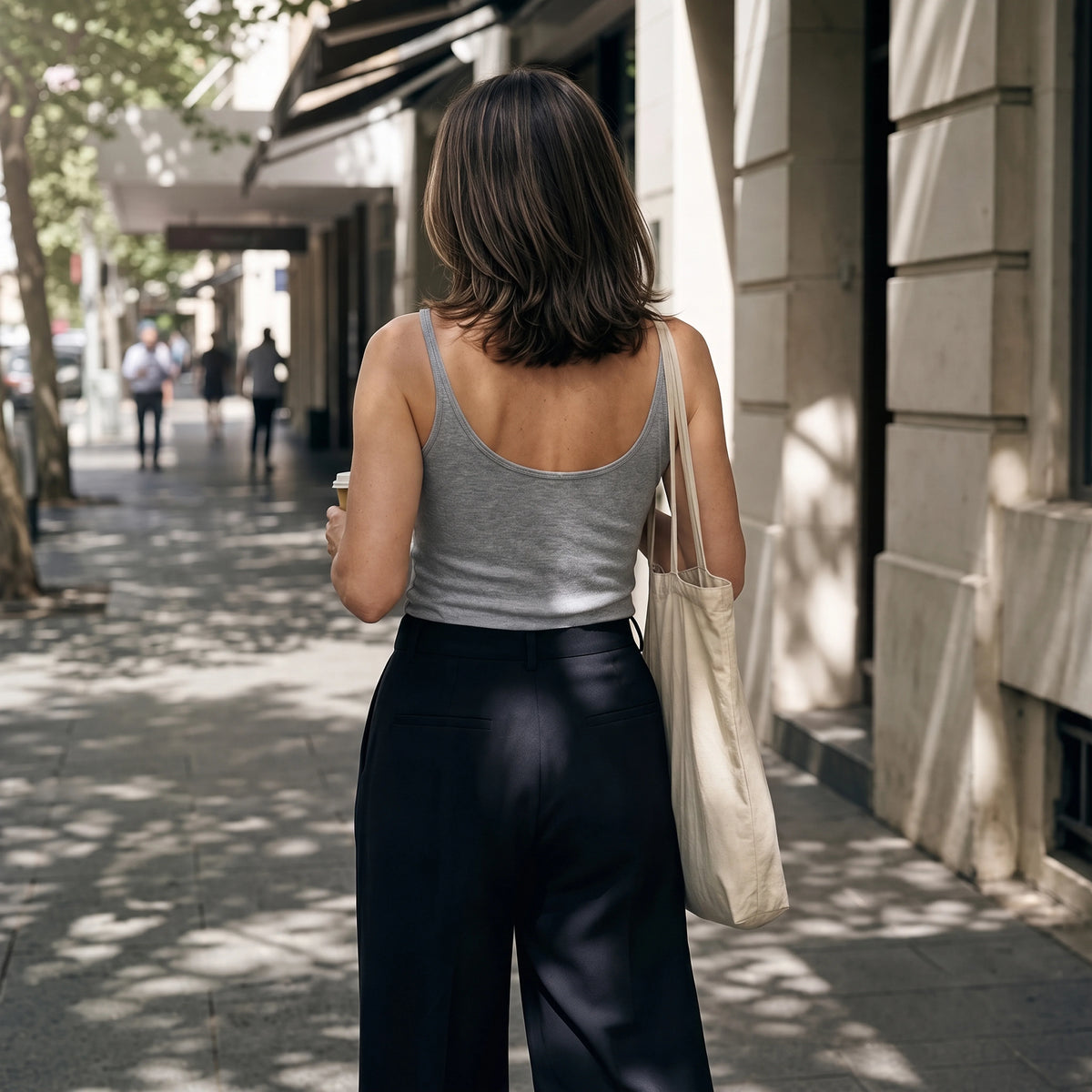Back view of a melange grey camisole with black tailored pants, carrying a canvas tote bag