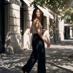 Woman looking over her shoulder in a melange grey built-in bra camisole and black wide-leg pants, holding a takeaway coffee