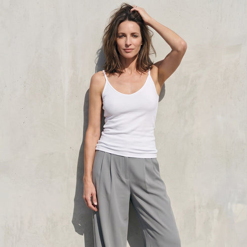 White built-in bra camisole with grey wide-leg tailored pants, one hand raised to her hair