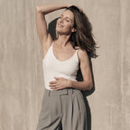 Close-up of a woman in a white built-in bra camisole and taupe pleated pants, face tilted up to the sun
