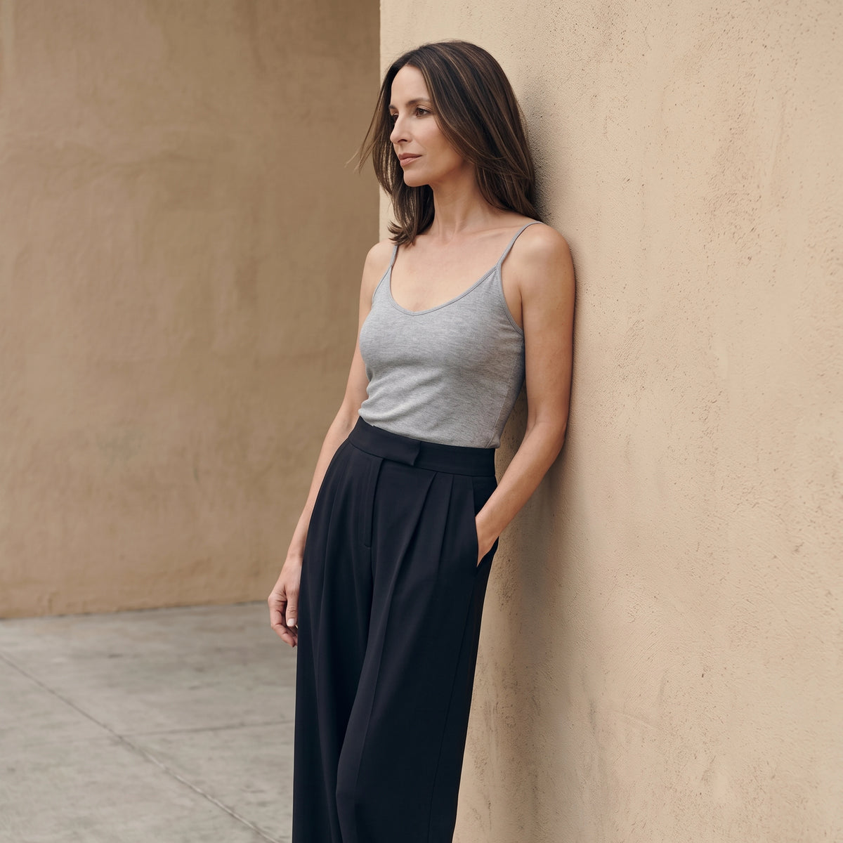 Le monde des hiboux built-in bra camisole in melange grey, worn with black wide-leg tailored pants, leaning against a warm sand-coloured wall