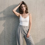 White built-in bra camisole with grey wide-leg tailored pants, one hand raised to her hair