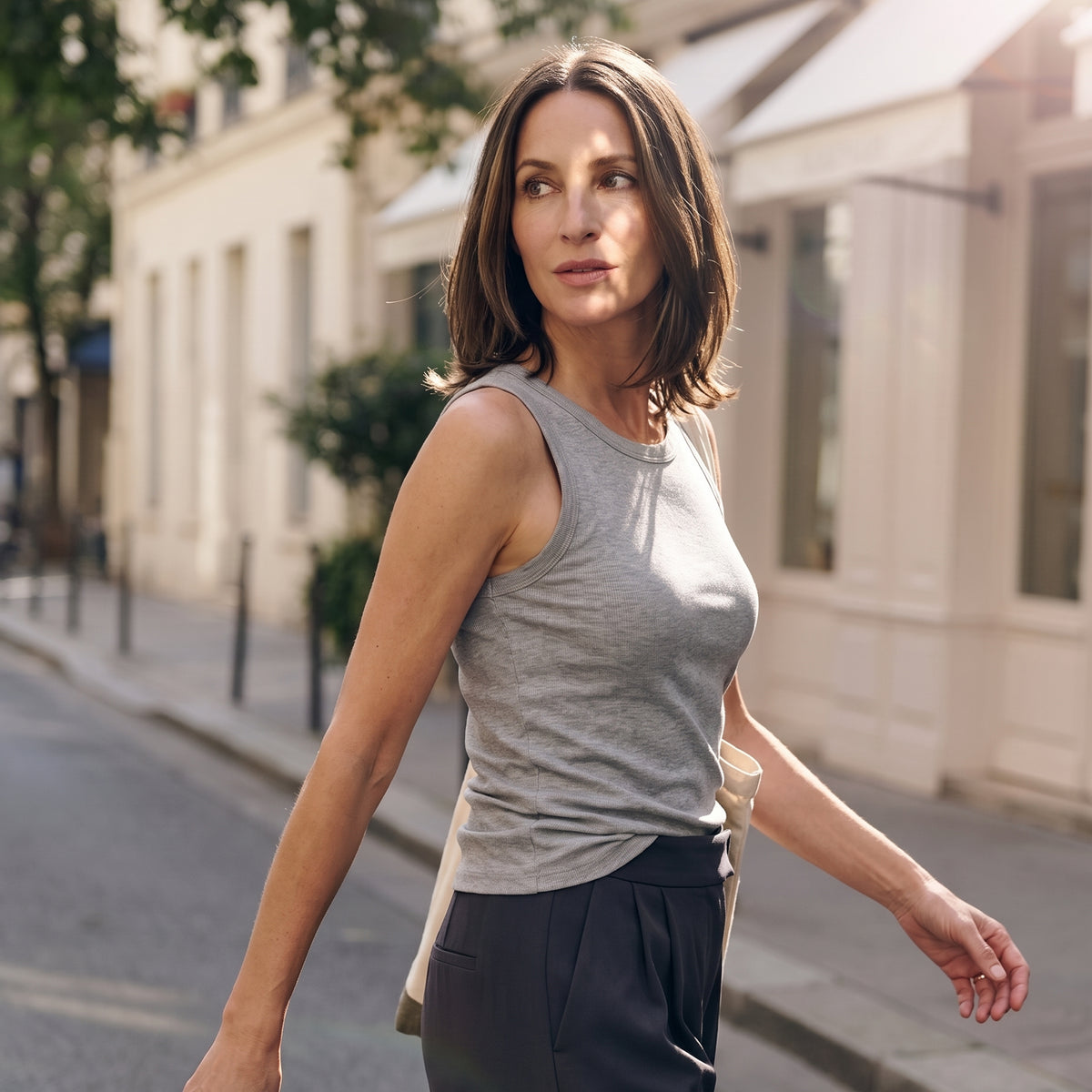 Woman walking in a melange grey built-in bra tank top and grey pleated pants with a canvas tote bag