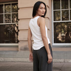 Back view of an off white tank top showing the round neckline and armhole, with dark grey pants