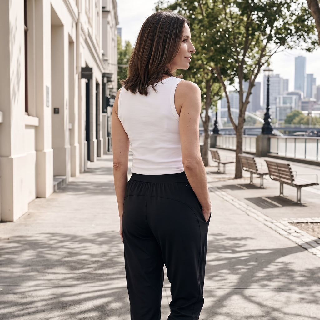 Back view of an off white tank top with black jogger pants, walking along a sunny path
