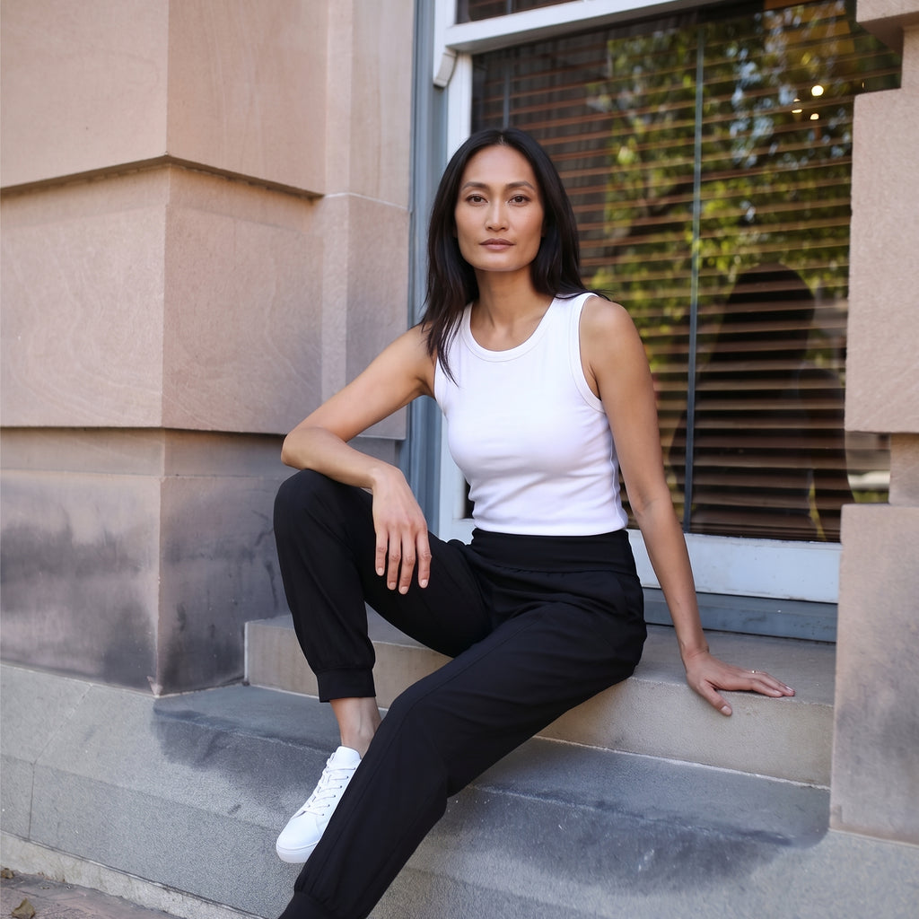 Le monde des hiboux built-in bra tank top in off white, worn with black jogger pants, seated on a step