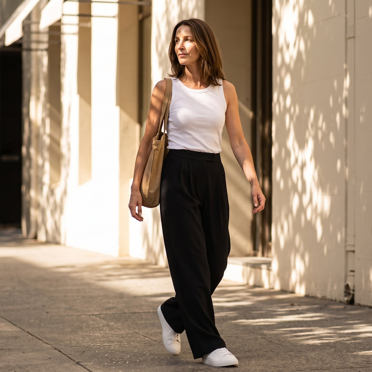 Woman walking in an off white built-in bra tank top and black wide-leg pants with a tan tote bag