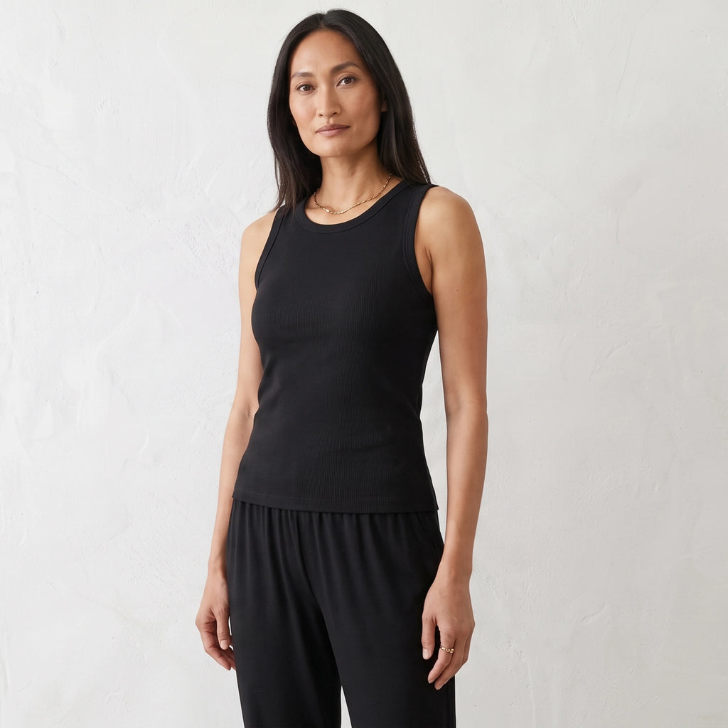 Black ribbed built-in bra tank top with a gold necklace against a white wall
