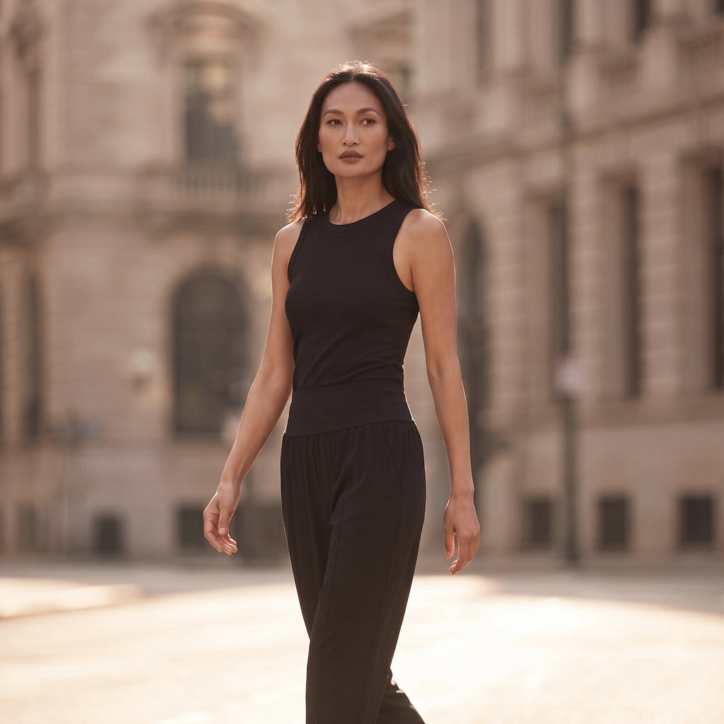 Woman walking in a black ribbed built-in bra tank top and black jogger pants in soft morning light