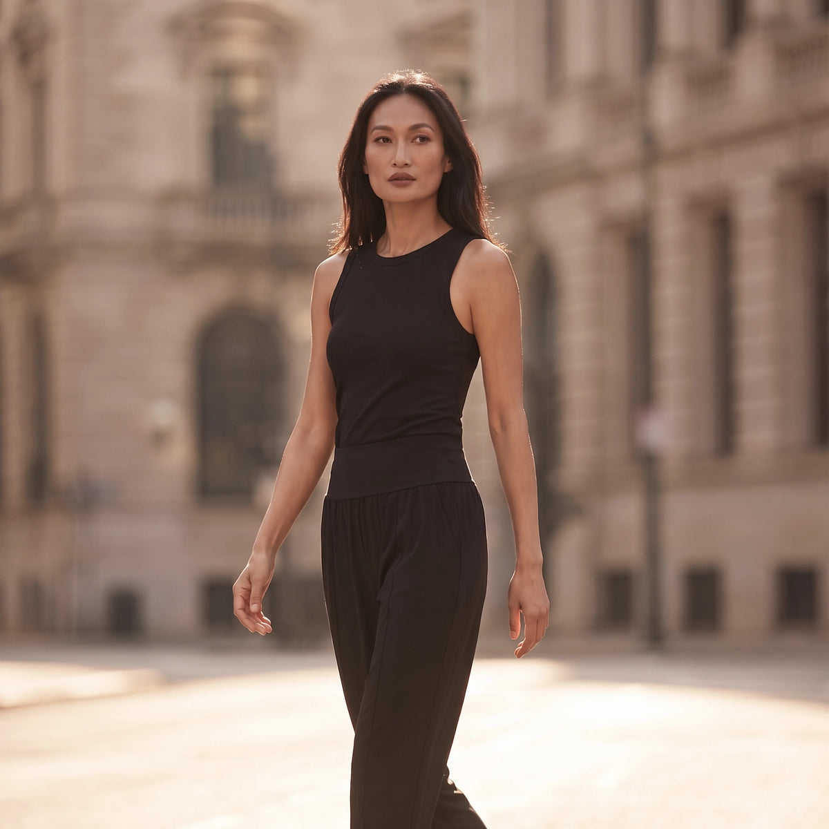 Woman walking in a black ribbed built-in bra tank top and black jogger pants in soft morning light