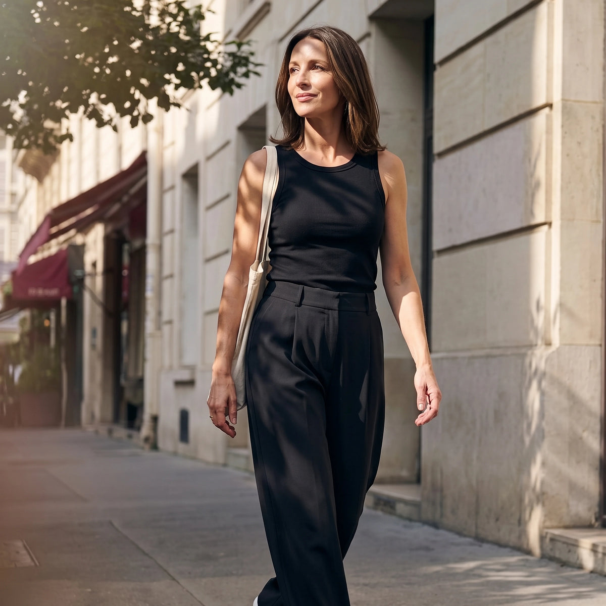 Woman walking in a black built-in bra tank top and black tailored pants with a canvas tote bag