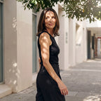 Black ribbed built-in bra tank top with black pleated pants, glancing over her shoulder in dappled sunlight
