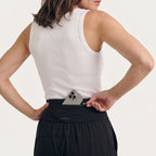 Back waistband of black jersey jogger pants with a hidden zip pocket holding a phone, worn with a white ribbed tank top