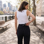 Woman sliding sunglasses into the hidden back zip pocket of black jersey jogger pants on a waterfront path
