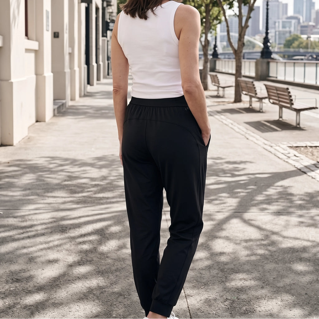Back view of black jersey jogger pants with a wide waistband and back seam detail, one hand in pocket