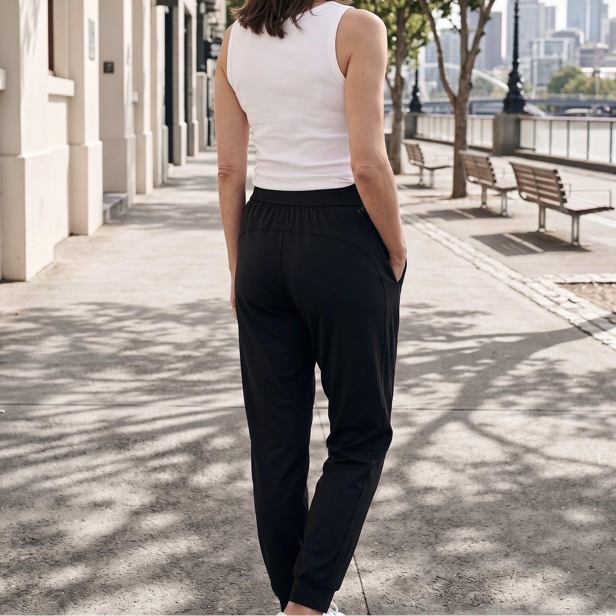 Back view of black jersey jogger pants with a wide waistband and back seam detail, one hand in pocket