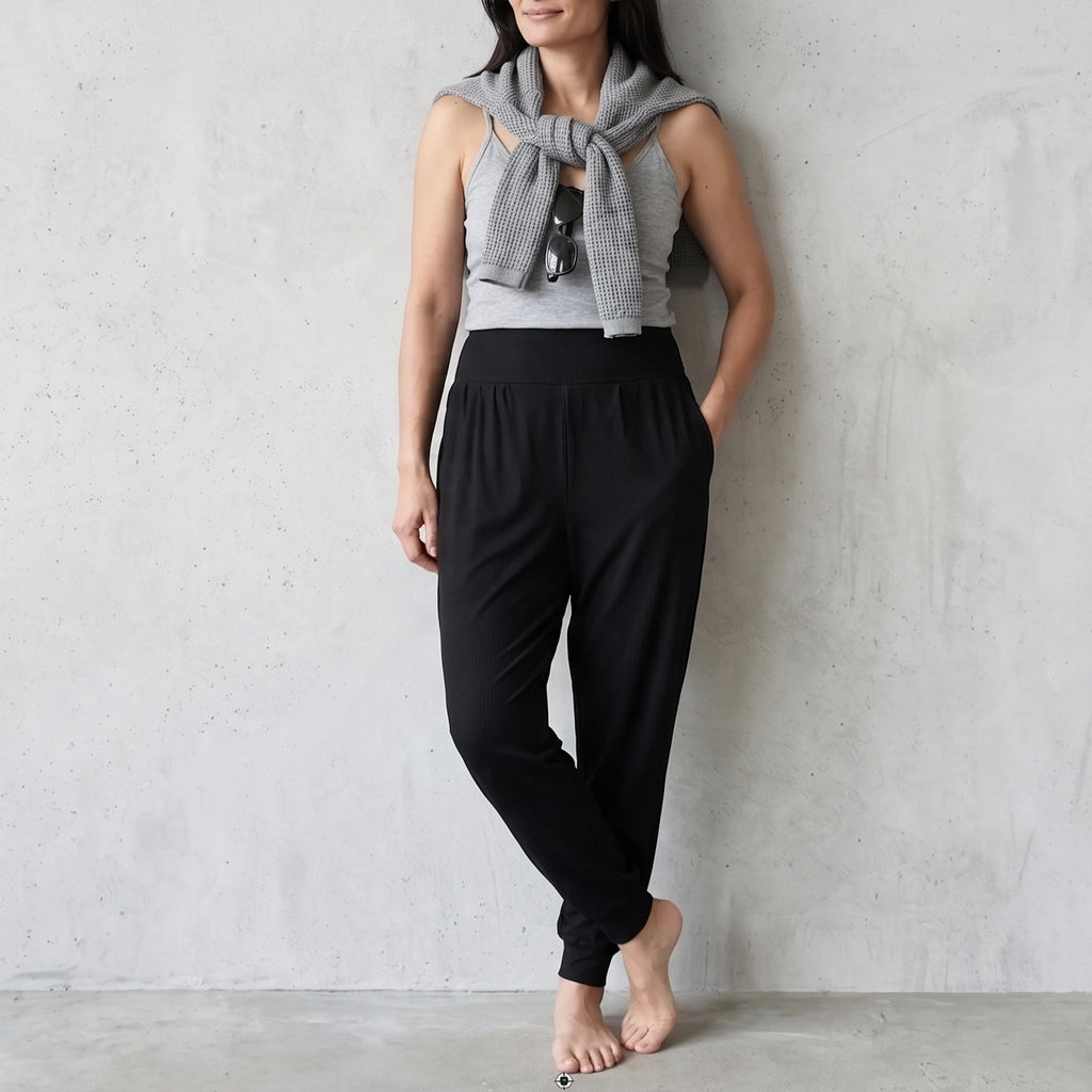 Black jersey jogger pants with ankle cuffs, styled with a grey camisole and a knit sweater tied over the shoulders