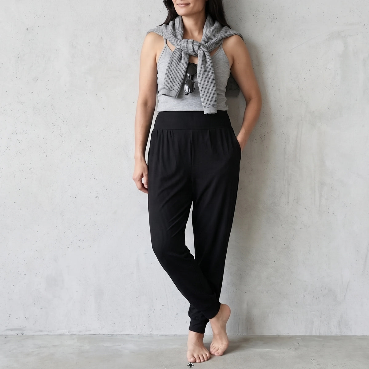 Black jersey jogger pants with ankle cuffs, styled with a grey camisole and a knit sweater tied over the shoulders