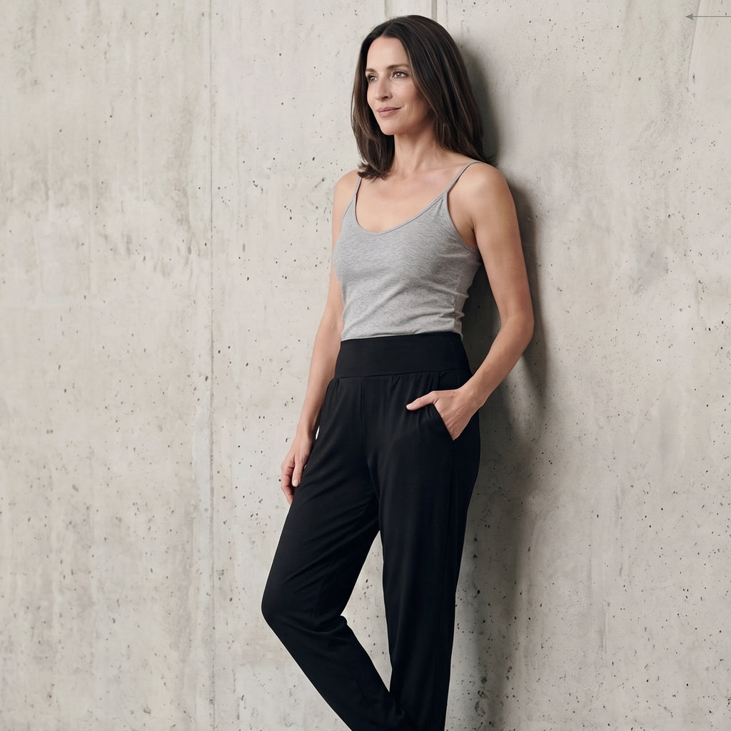 Black jersey jogger pants with a wide waistband and side pocket, styled with a grey camisole against a concrete wall