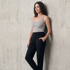 Black jersey jogger pants with a wide waistband and side pocket, styled with a grey camisole against a concrete wall