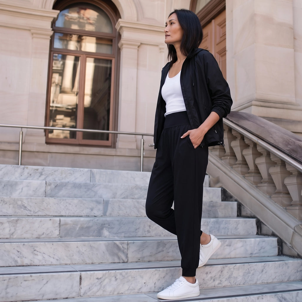 Woman in black jersey jogger pants, a black zip jacket and white sneakers walking down marble steps