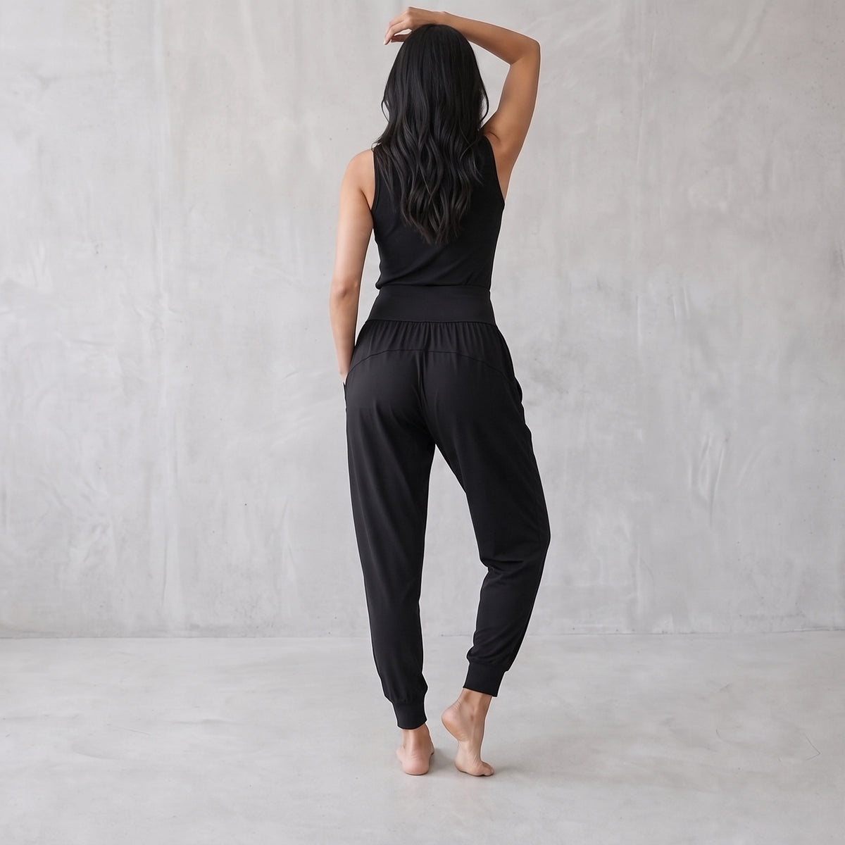Back view of black jogger pants with a wide waistband and ankle cuffs, one arm raised