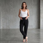 Black woven jogger pants with a wide high waistband, styled with a white camisole in a concrete-toned studio