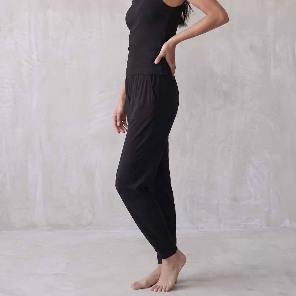 Side view of a black ribbed tank top and black jogger pants, hand on hip