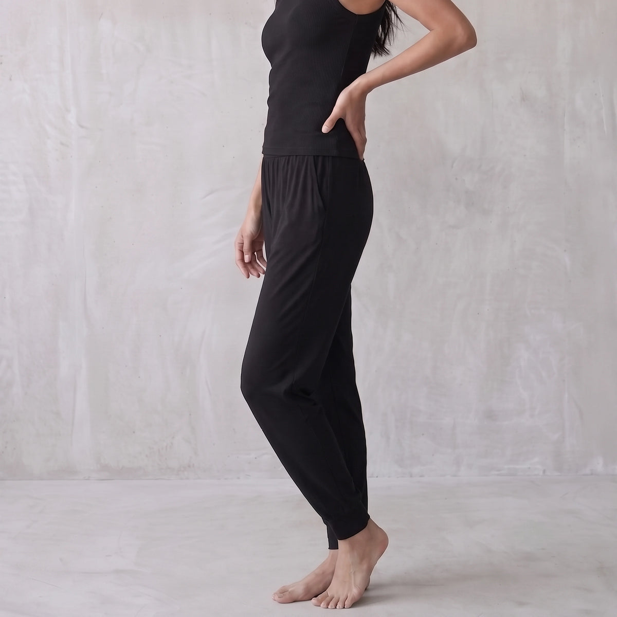 Side view of a black ribbed tank top and black jogger pants, hand on hip