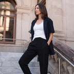Woman in black woven jogger pants, a navy blazer and a white camisole, with one hand in her pocket